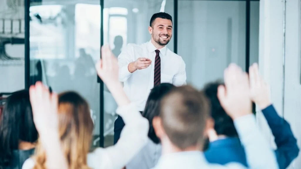 Formateur animant un atelier devant un groupe, mains levées